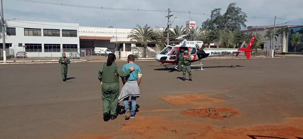 Foto exibe duas pessoas se aproximando de helicóptero pousado.