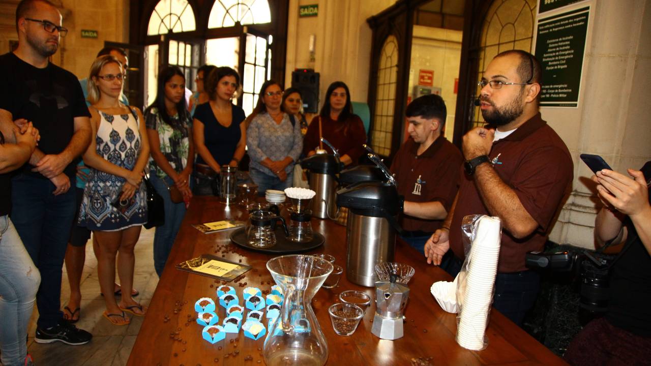 Um funcionário faz uma apresentação próximo a uma mesa com cafés e doces