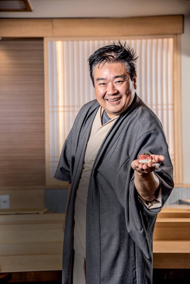 Edson Yamashita segura sushi e sorri para a câmera