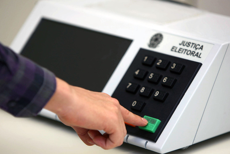 Imagem mostra uma pessoa apertando a tecla 'confirma' na urna eletrônica.