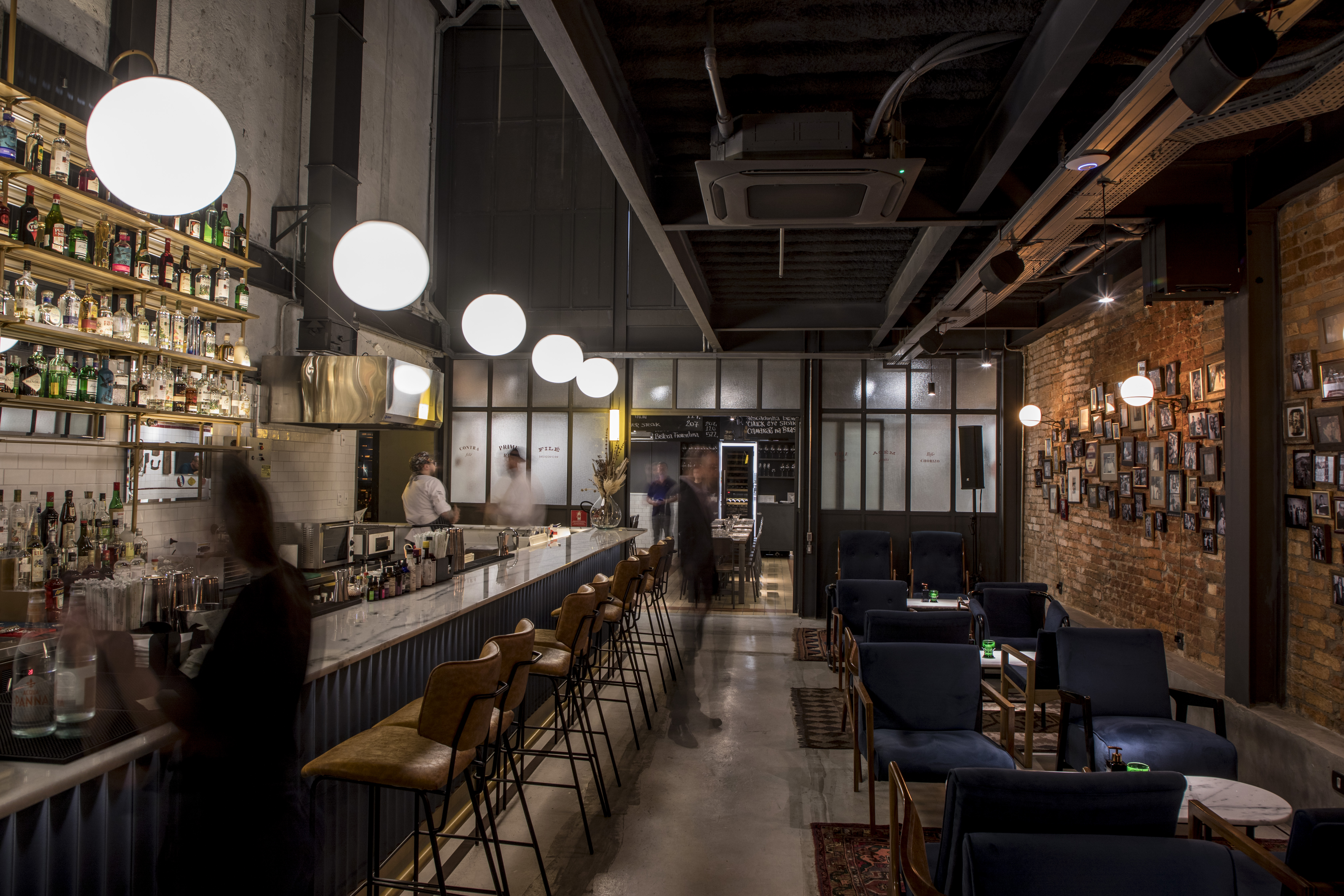 Balcão de bar, com mesas à direita e lustras pendurados