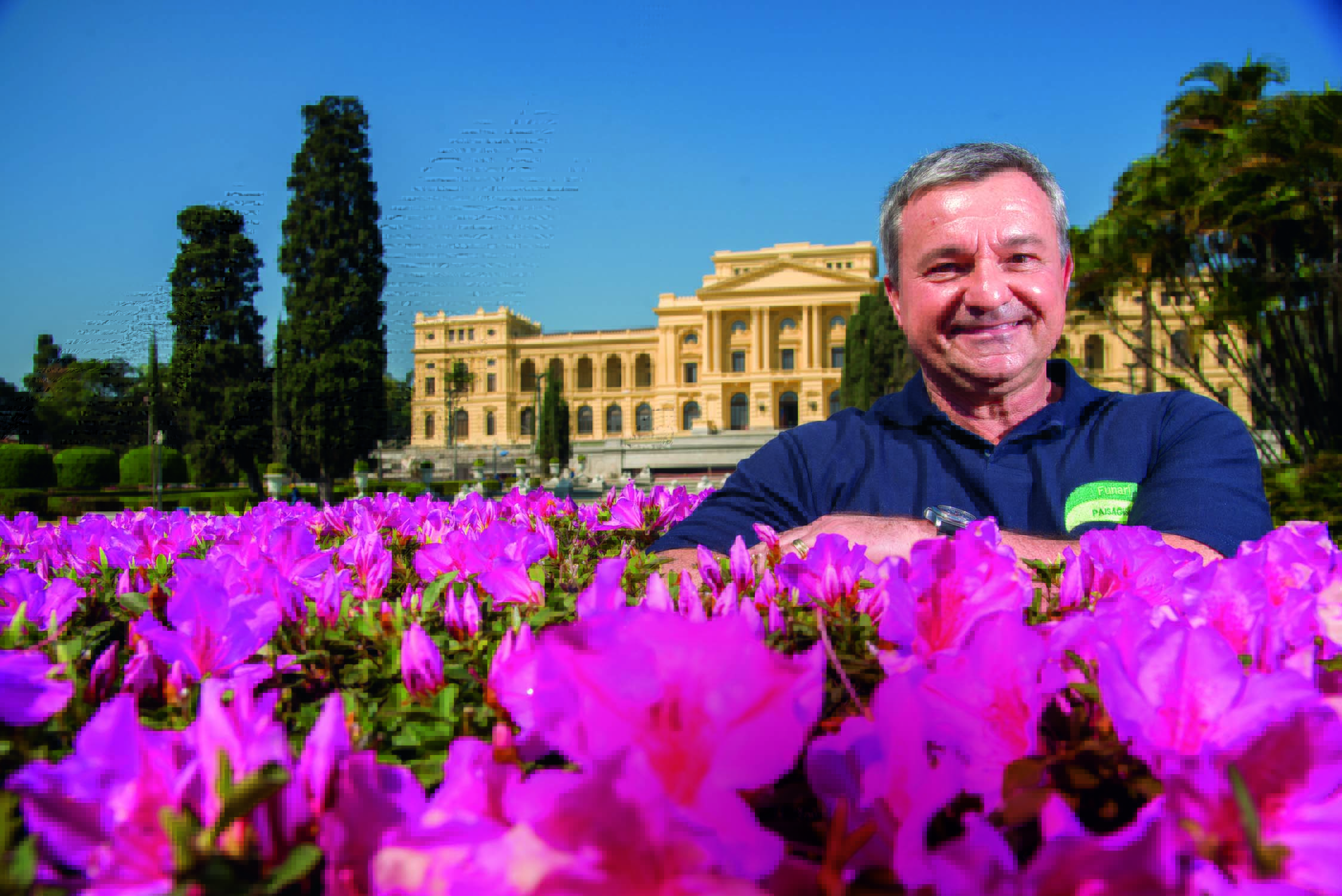 Eduardo Funari, paisagista do jardim do Museu do Ipiranga, posa atrás de rosas e com o Museu ao fundo.