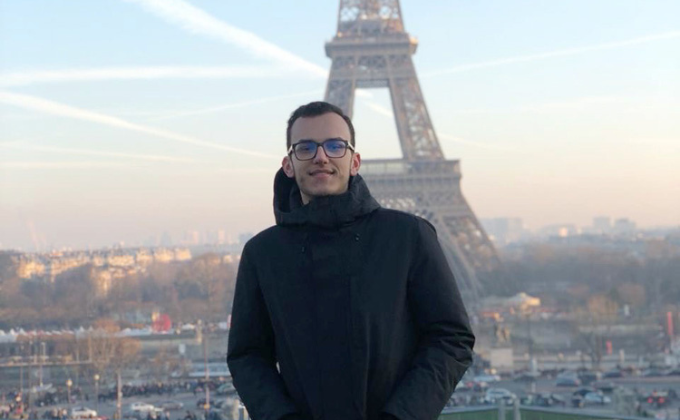 Imagem mostra homem de casaco preto com a Torre Eiffel ao fundo, em Paris