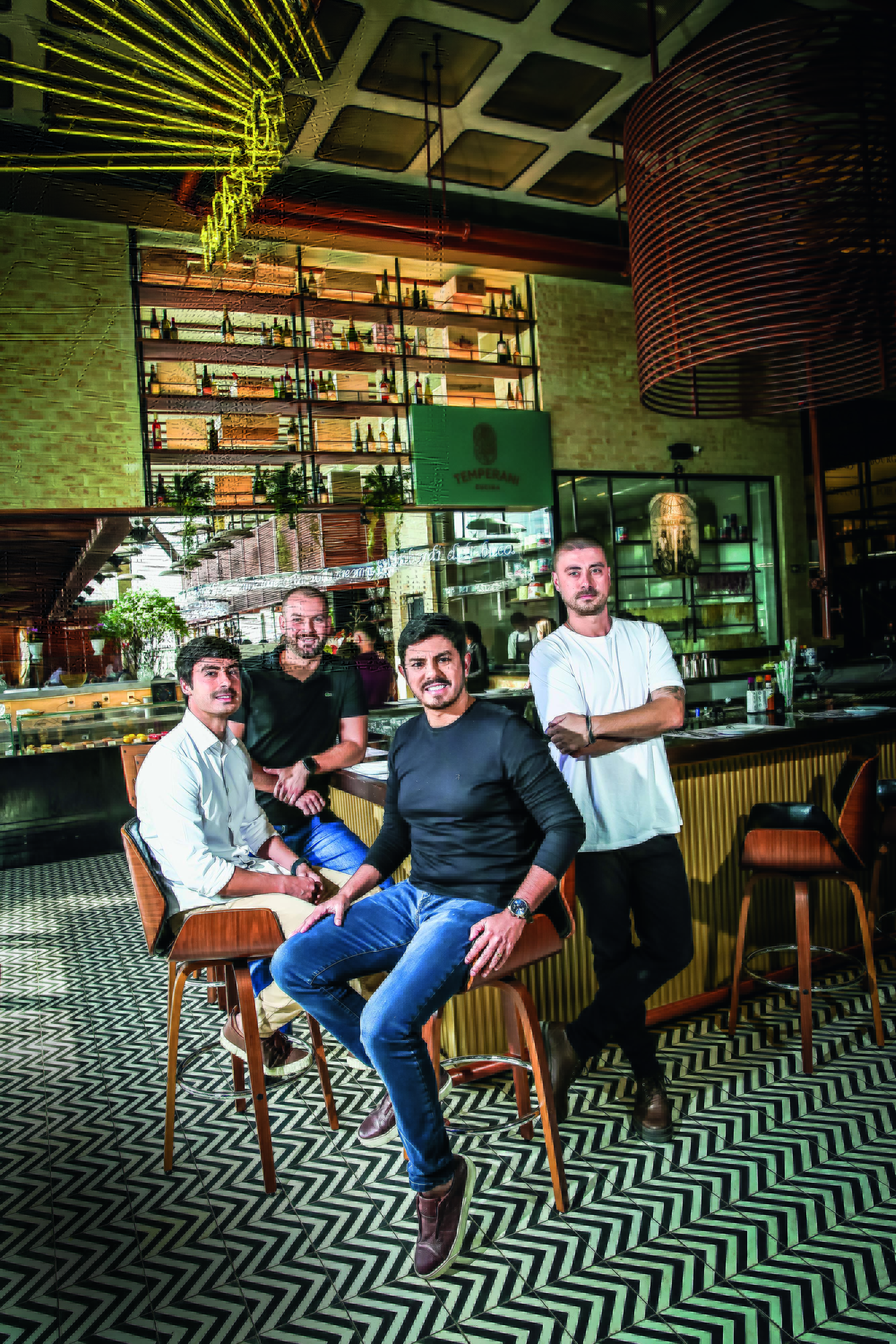 Imagem mostra quatro homens sorrindo sentados em bar de restaurante