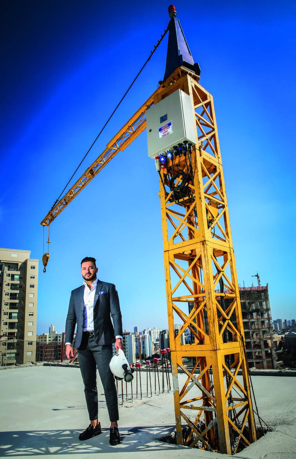 Imagem mostra homem de terno em terreno de construção. Ao fundo, um andaime amarelo.