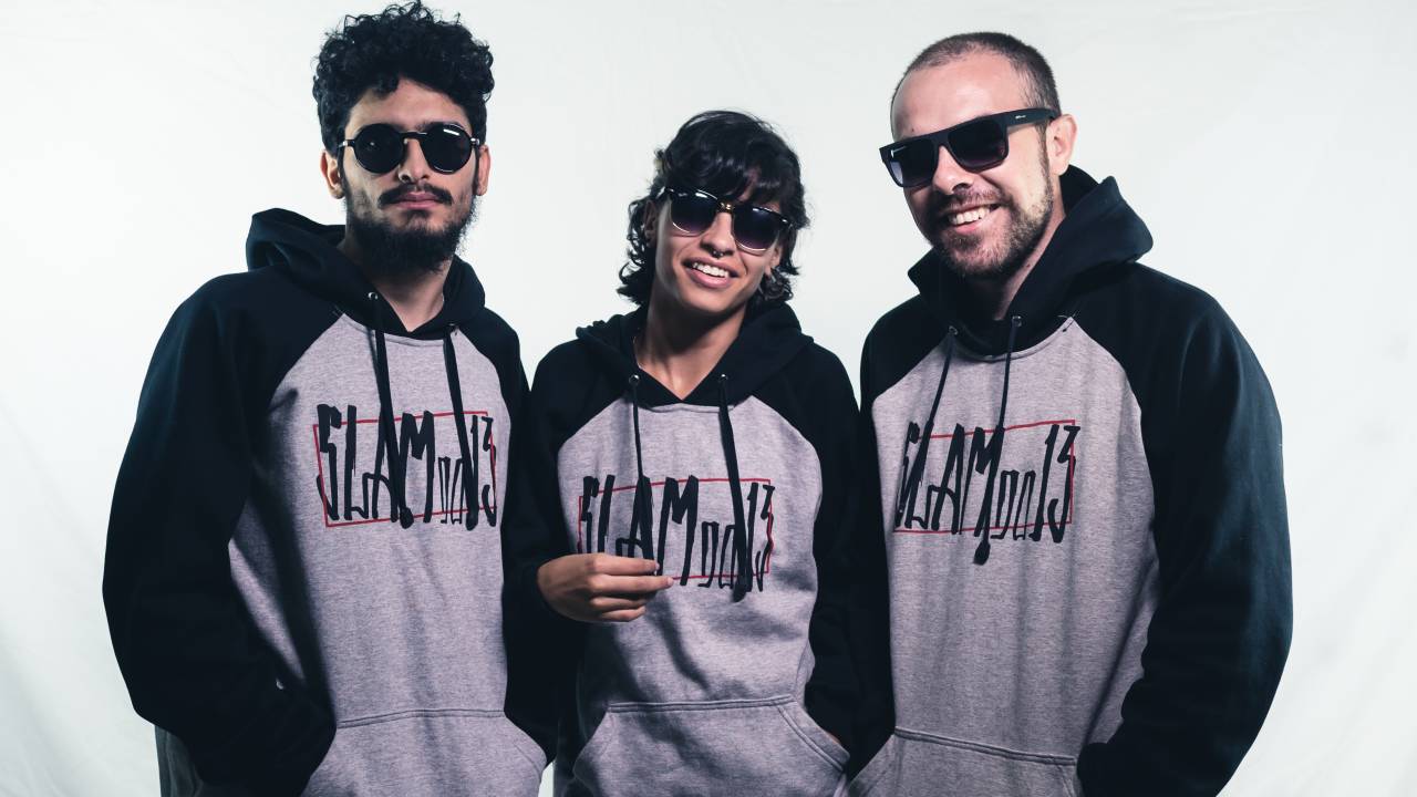 Três pessoas de moletom cinza e óculos escuros posam para a foto sorrindo.