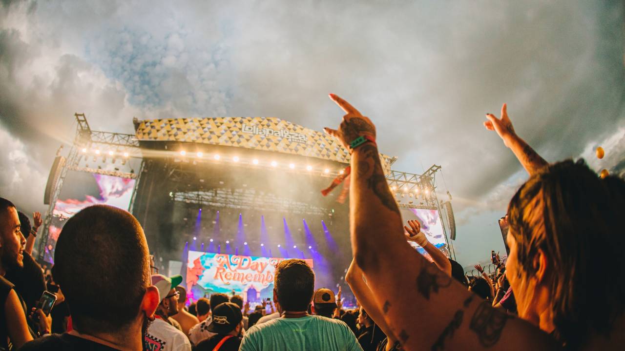 Imagem mostra em primeira plano multidão de pessoas com braços levantados olhando para palco ao fundo, com apresentação de artista no Lollapalooza