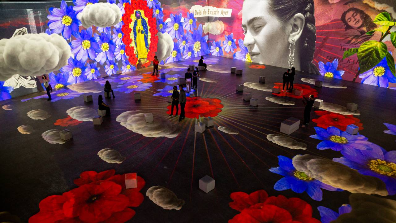 Foto de ambiente com projeções coloridas que remontam obras de Frida Kahlo e imagem da artista
