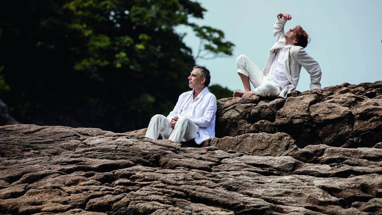 Imagem mostra dois homens de roupas brancas em cima de pedra