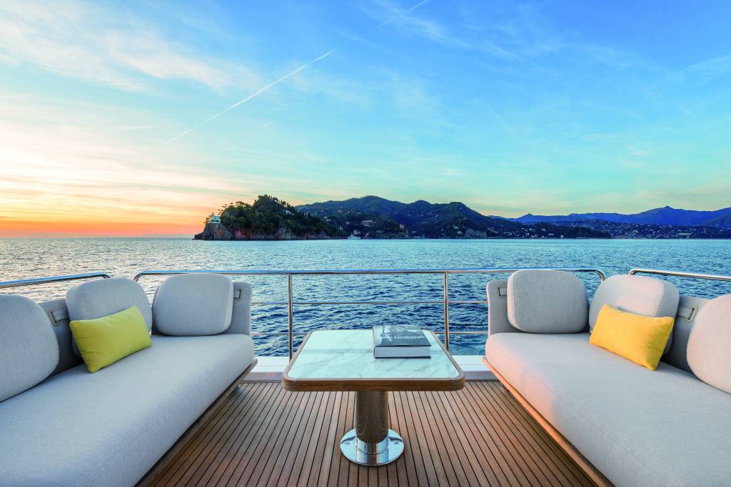 Azimut 62 (Divulgação Azimut Yachts) (4) Foto de varanda com sofás brancos e mesinha em iate. Ao fundo, o mar e uma ilha.