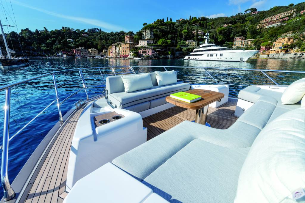 Azimut 62 (Divulgação Azimut Yachts) (5) Foto de canto de iate com sofás brancos, mesinha e vista para o mar e ilha ao fundo.