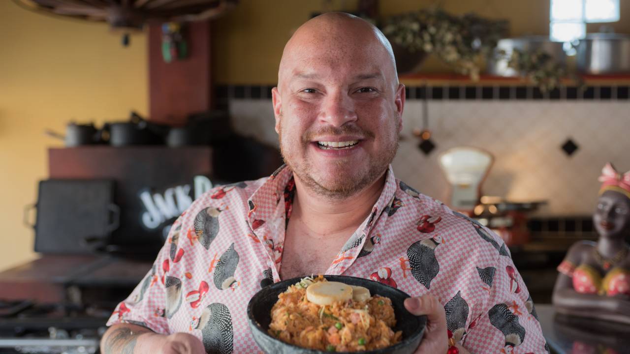 Bruno Salomão, homem branco e careca, sorri para a foto segurando prato com comida.