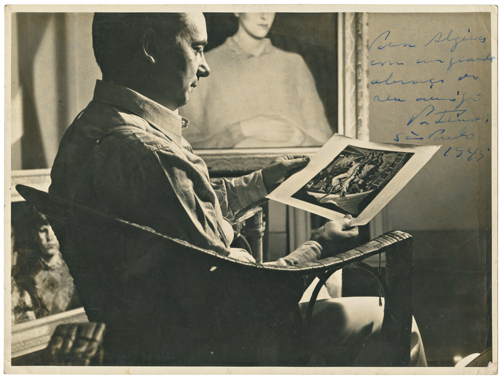 Imagem mostra homem sentado em cadeira, vendo pintura em papel
