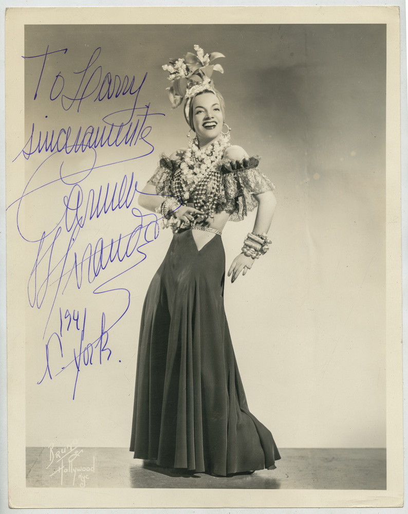 Imagem em preto e branco mostra mulher de vestido e chapéu tropical, dançando