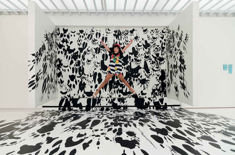 Menina pula em frente a mural com pegadas pretas de animais