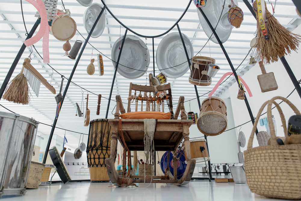 Instalação de arte circular, com instrumentos diversos em volta. Há uma cadeira de balanço no meio