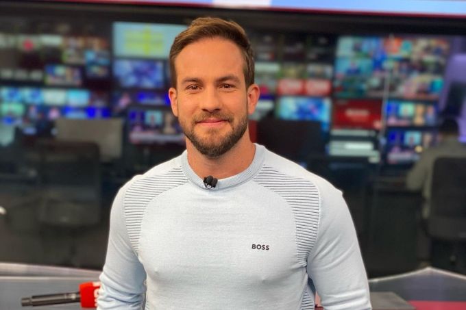 Foto de Daniel Adjuto usando suéter branco, sorrindo, no estúdio do Live CNN