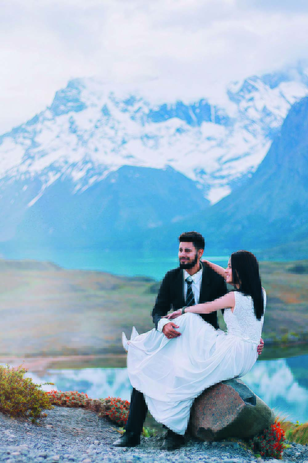 Pamela e Douglas sentados em uma pedra em uma montanha da Patagônia. Ela usa um vestido de casamento e ele um terno
