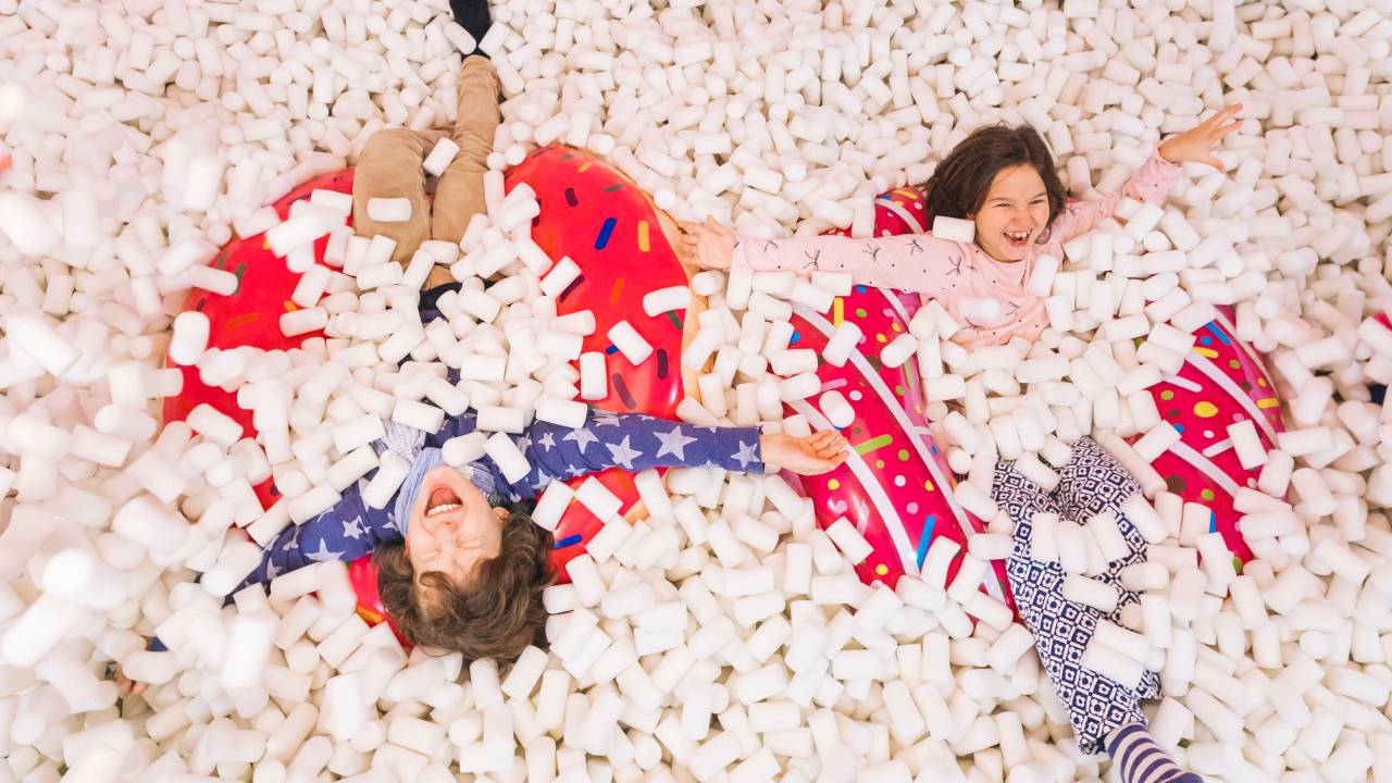 Duas crianças aparecem deitadas em piscina de marshmallows de mentira.