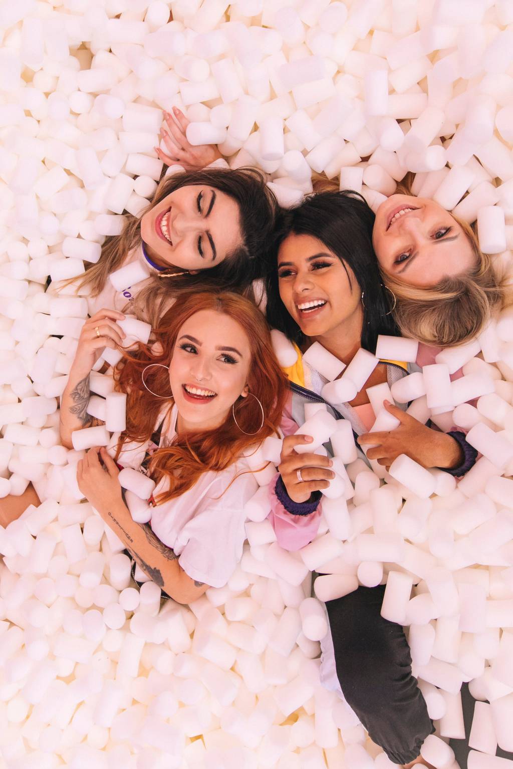 Quatro moças sorriem para a câmera cobertas por marshmallows de mentira em uma piscina.