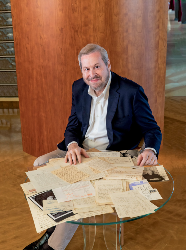 Imagem mostra homem grisalho de terno sentado em mesa com diversos documentos e cartas