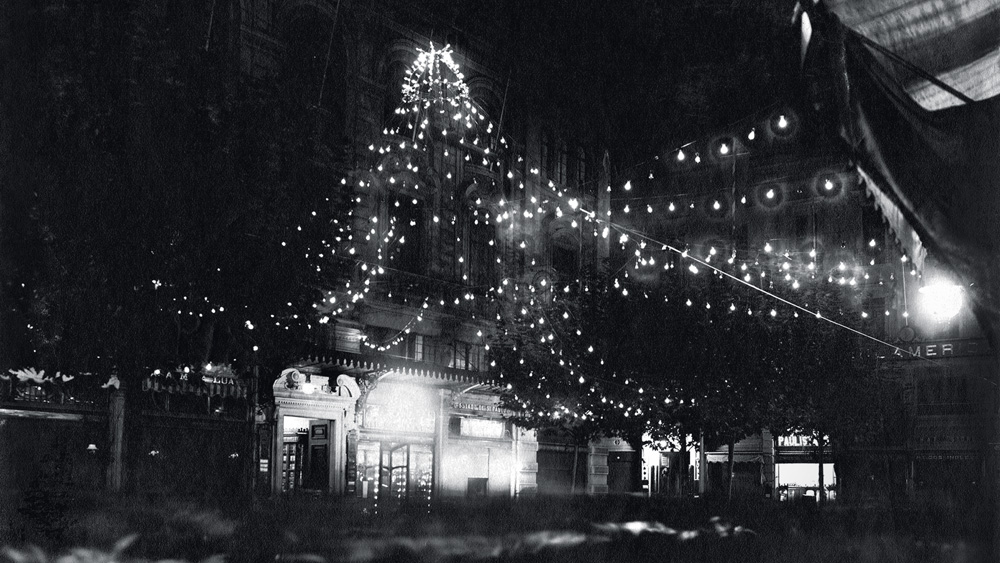 Imagem em preto e branco mostra prédio com luzes decorativas que se estendem até a rua