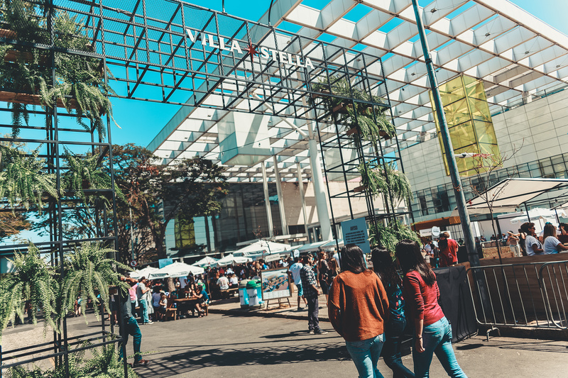 Entrada de evento ao ar livre com pessoas andando em direção a um arco de metal.