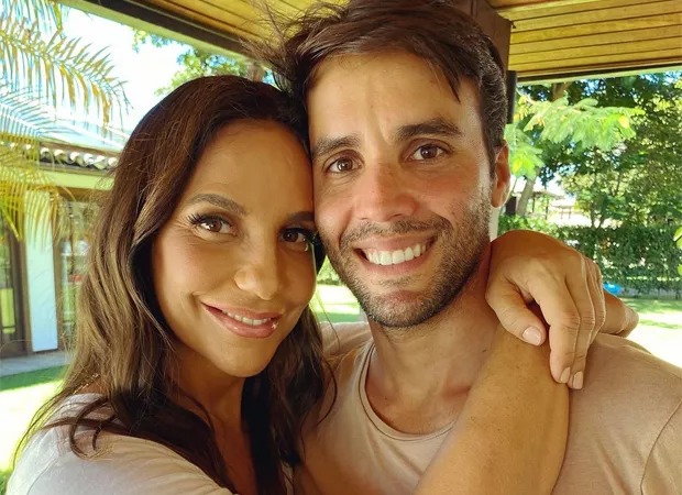 Ivete Sangalo posa abraçada com as mãos envoltas nos ombros de Daniel Cady, sorrindo, diante de fundo com árvores e que parece uma casa