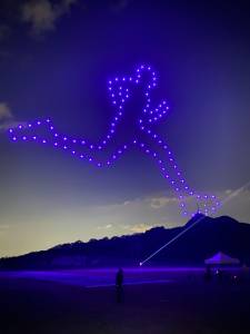 Foto mostra drones iluminados no céu em formato de silhueta de uma pessoa fazendo exercício físico.