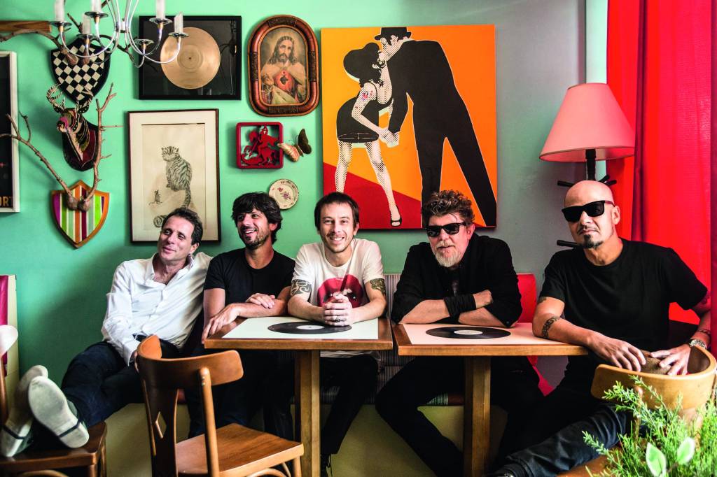 crédito Silmara Ciuffa_Divulgação.jpg Imagem mostra cinco homens sentados ao redor de mesas, em ambiente com quadros coloridos na parede