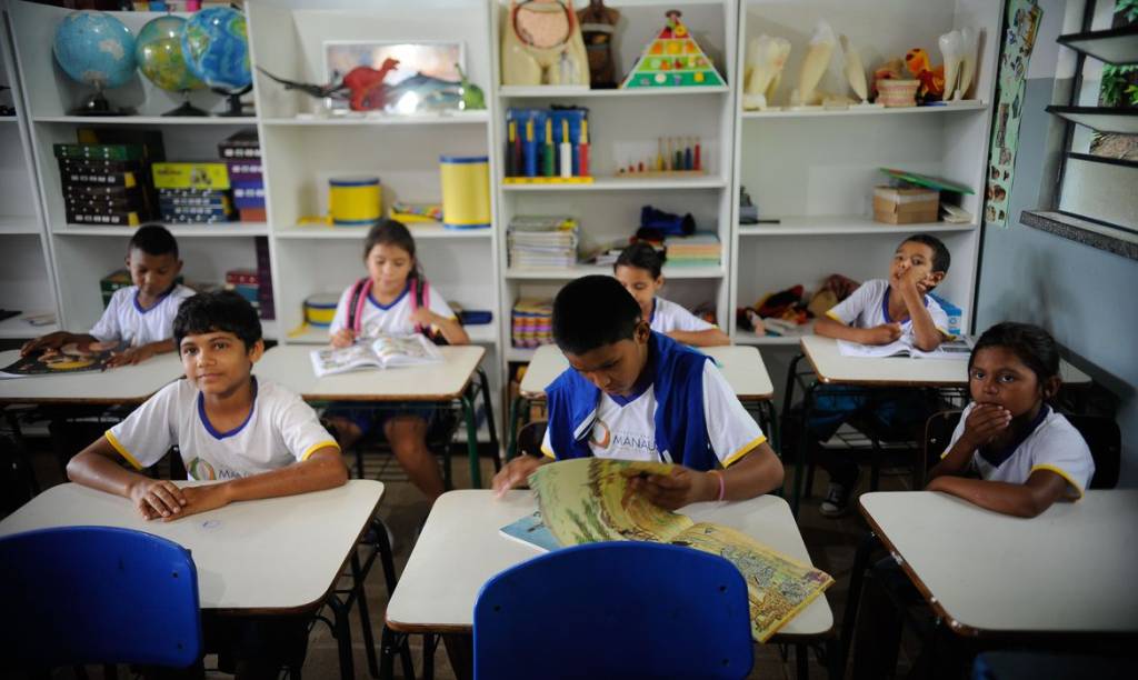 Foto mostra cinco alunos sentados em carteiras dentro da sala de aula.