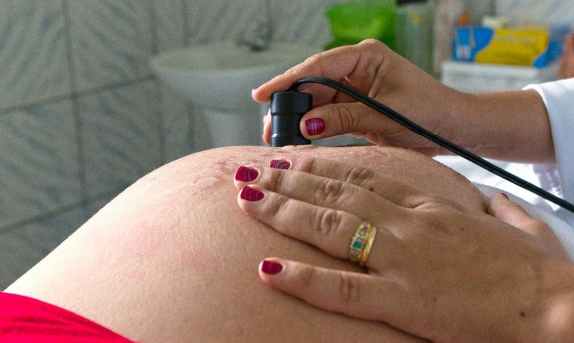 Foto de barriga de gestante com mãos de médica sobrepondo a barriga com equipamento para exame