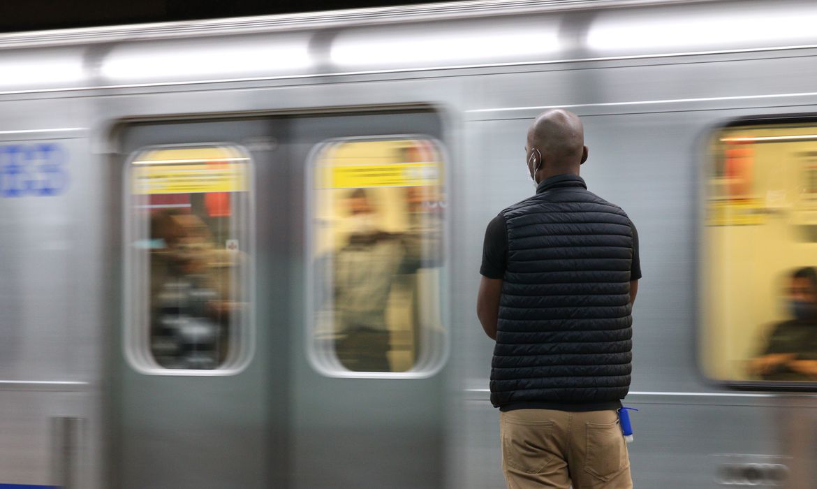 Homem espera metrô parar para entrar no vagão, que está em movimento