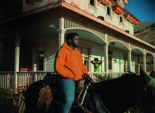 Imagem mostra homem vestindo casaco laranja e calça jeans em cima de cavalo