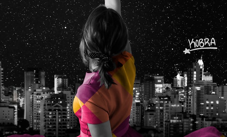 Uma menina de costas tenta alcançar as estrelas com a mão
