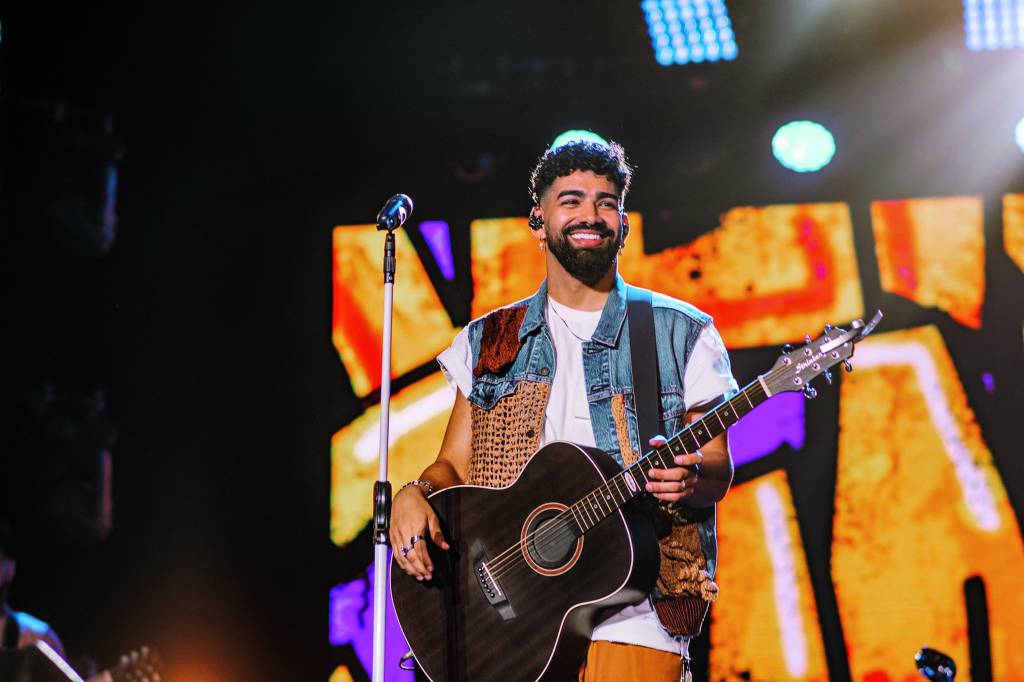 Foto de Dilsinho durante apresentação, segurando violão e sorrindo para a plateia