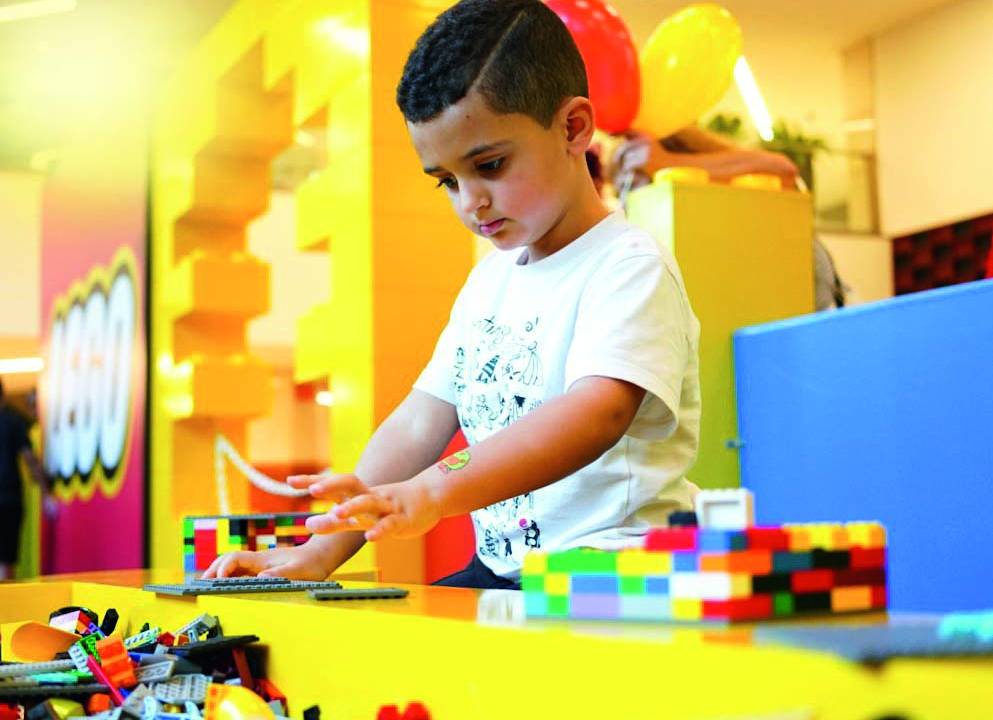 Menino negro monta peças de LEGO em bancada amarela