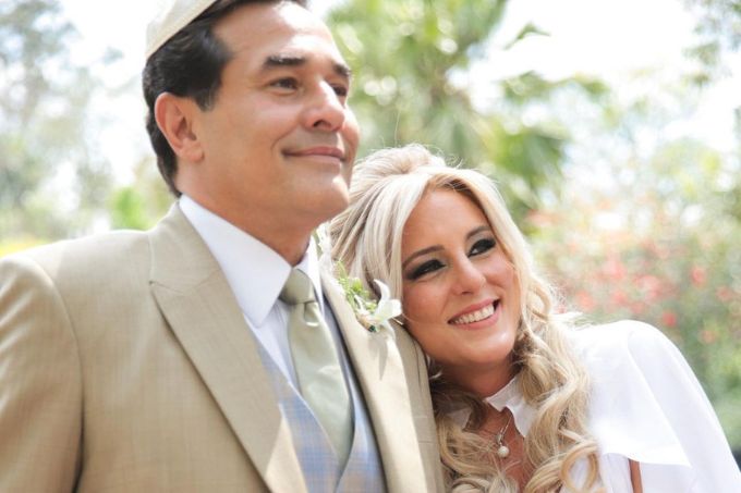 Foto de Luciano Szafir e Luhanna Melloni, usando terno e vestido de casamento, sorrindo olhando para a direita