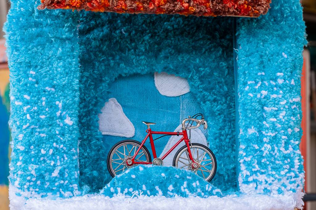 Liberdade_céu _ sótão Miniatura de casinha azul estofada por dentro. No fundo, há um céu com nuvens e, na frente, uma pequena bicicleta vermelha
