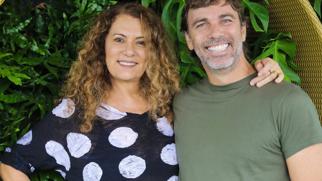 Patricya Travassos e Marcelo Faria sorriem para a câmera abraçados, ela veste camiseta preta de bolas brancas e ele camiseta básica verde.