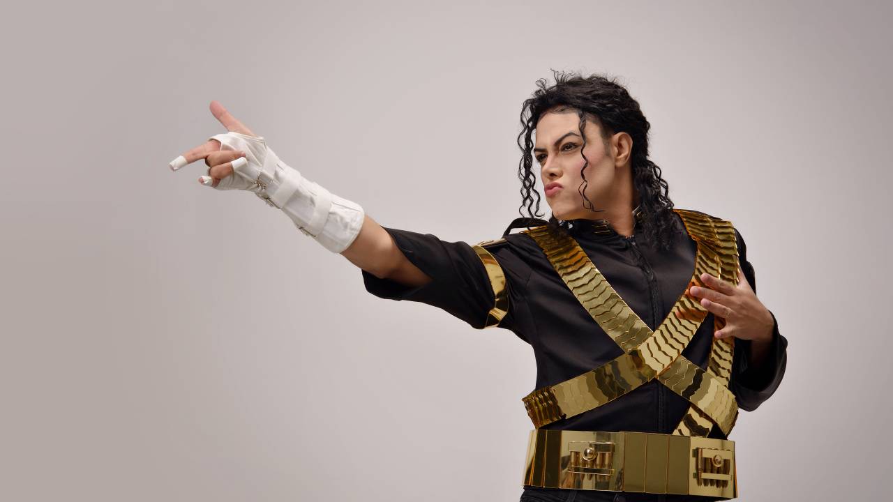 Rodrigo Teaser, intérprete de Michael Jackson, posa com dedo em riste e roupa preta e dourada.