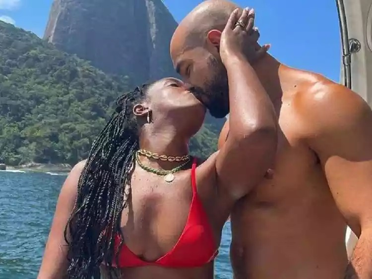 Foto de Iza e Sérgio Santos em barco, diante do Pão de Açúcar, se beijando, usando roupa de praia