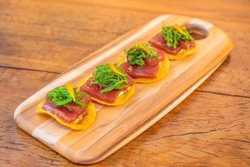 Quatro tostadas de milho com atum marinado sobre elas, dispostas sobre uma tábua de madeira para servir