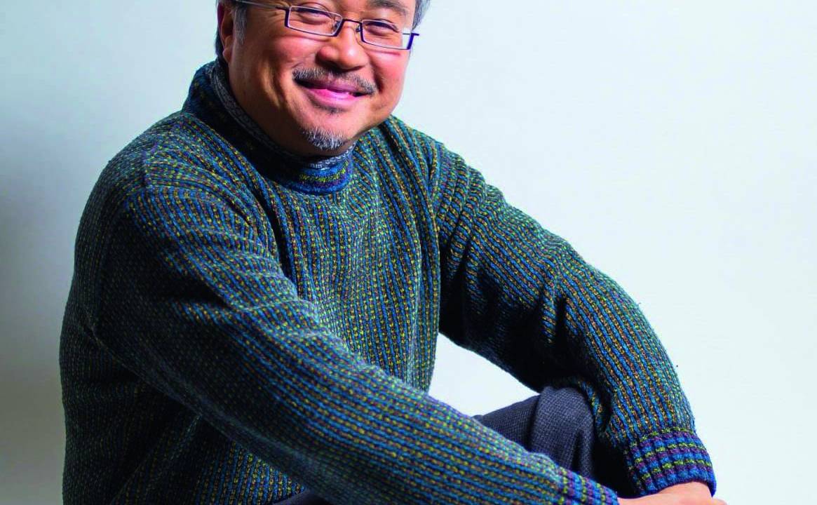Foto de Dang Thai Son sentado no chão de estúdio, sorrindo, usando suéter e calça