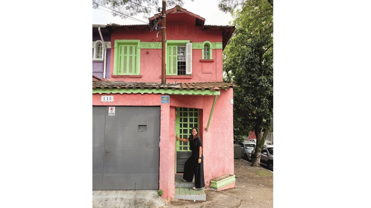 Manuelle Ferraz de preto em frente ao portão de casa rosa e verde