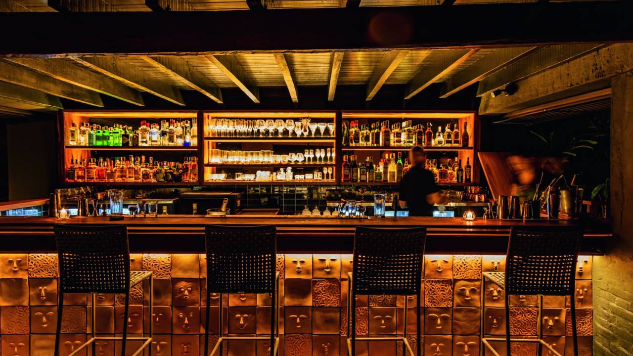 Ambiente interno do Bar do Manacá com balcão, banquetas e estantes com bebidas