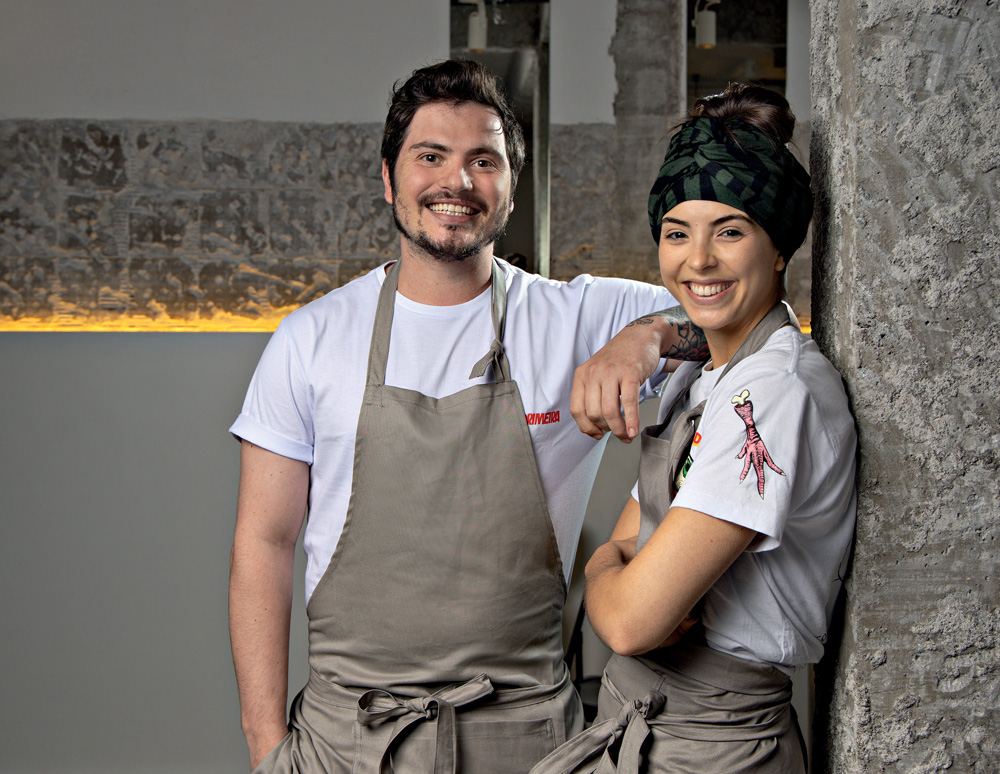 Imagem mostra homem e mulher sorrindo, ambos com avental bege sobre camiseta branca