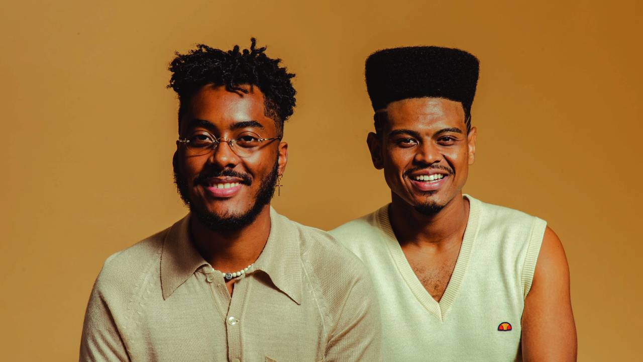 Imagem mostra dois homens sobre fundo amarelo, sorrindo