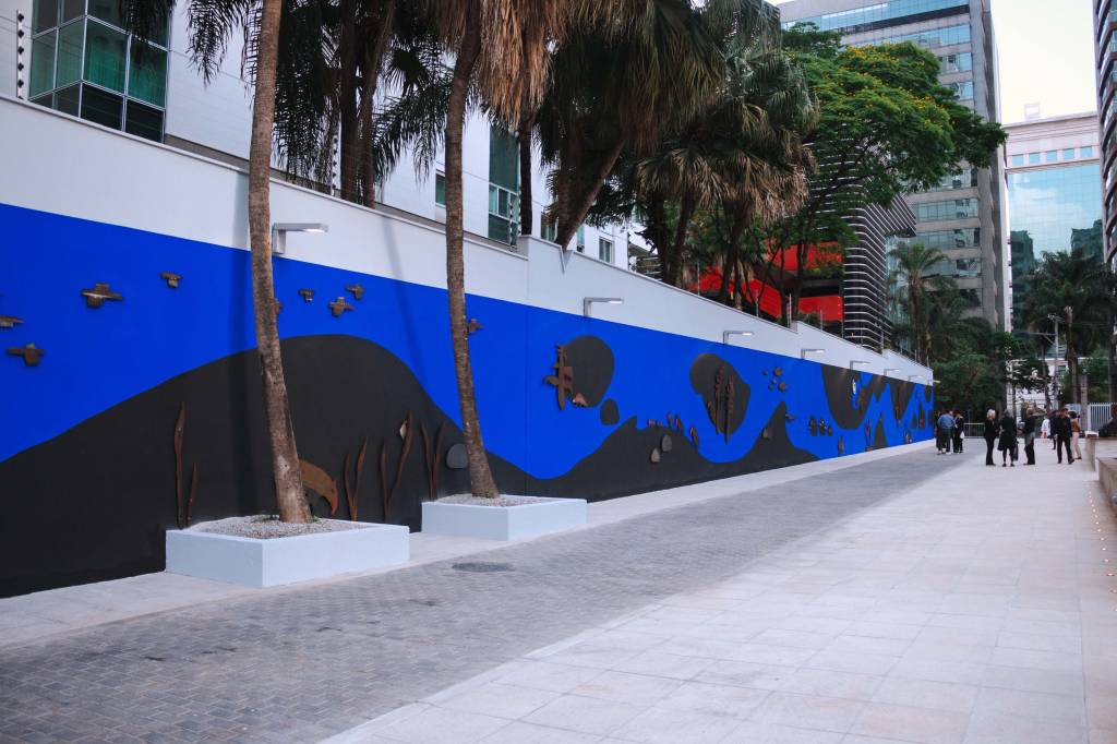 Muro comprido com mural azul repleto de peças de aço enferrujado que simbolizam animais