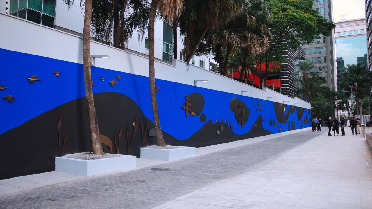 Muro comprido com mural azul repleto de peças de aço enferrujado que simbolizam animais